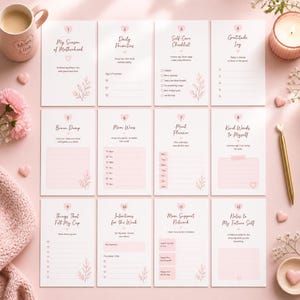 以下が含まれることがあります： 「My Season of Motherhood」や「Daily Priorities」などの見出しが付いた、ピンクと白のセルフケアジャーナルカード12枚のセット。マグカップ、キャンドル、ペンも写っています。