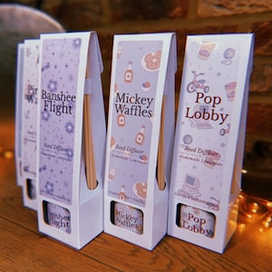 May include: Several reed diffusers in white boxes with lavender and white designs. The boxes have text that reads "Banshee Flight", "Mickey Waffles", and "Pop Lobby". Each box contains reed sticks and a small cylindrical container.