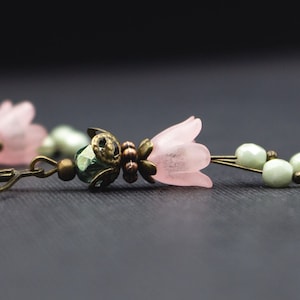 May include: A pair of pink flower earrings with green and bronze beads. The earrings have a hook closure.