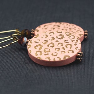 May include: A pair of pink leopard print earrings with gold hoops and brown beads.