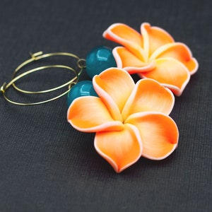 Może przedstawiać: Para złotych kółek z pomarańczowymi kwiatowymi zawieszkami i turkusowymi koralikami.