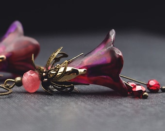 May include: A pair of earrings featuring a pink flower design with gold accents and a pink stone. The earrings have a hook closure.