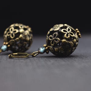 May include: A pair of gold-toned earrings with intricate floral designs and blue gemstone accents.