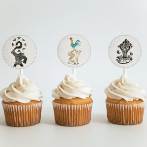 May include: Three cupcakes with white frosting and decorative toppers. The toppers feature black and white illustrations of characters. The cupcakes are on a white surface, creating a clean and appealing presentation. Perfect for a themed party or celebration.