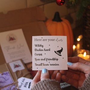 May include: A close-up of a card with the text "Here are your clues" and a list of clues: "Witchy", "Broken heart", "Curses", "Love and friendship", and "Small town reunion". The card is held in a hand with light blue nail polish.