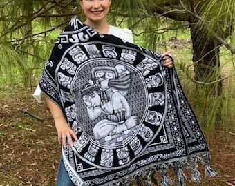 May include: A black and white woven shawl with a fringe border. The shawl features a central design of a figure with a headdress and a circular pattern of smaller figures around it.