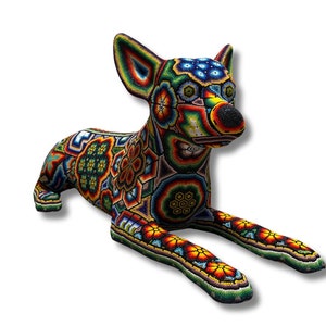 Puede incluir: Una figurita de chihuahua de cuentas de colores, acostada con la cabeza girada hacia un lado. La figurita está cubierta de intrincados patrones y diseños, incluyendo flores, formas geométricas y espirales. El chihuahua está hecho de cuentas de varios colores, incluyendo rojo, azul, verde, amarillo y naranja.