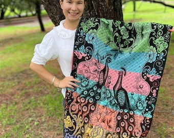May include: A colorful woven shawl with a peacock design and floral accents. The shawl has a black background with stripes of pink, blue, green, and yellow. The shawl has fringe on the bottom.