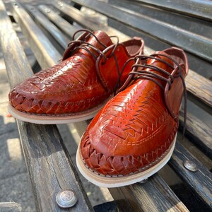 May include: A pair of brown leather shoes with intricate woven designs. The shoes have a white sole and brown laces.