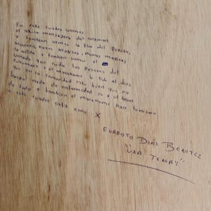 Może przedstawiać: Jasna drewniana deska z odręcznym tekstem wykonanym ciemnym tuszem. Napis zawiera szczeg&oacute;łową hiszpańską narrację o symbolach duchowych oraz podpis Evaristo D&iacute;az Benitez z tytułem Uxa Temay podkreślonym poniżej.