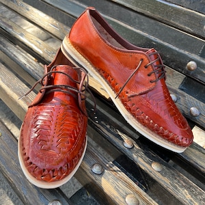 May include: A pair of brown leather shoes with woven detailing. The shoes have a lace-up closure and a white sole.