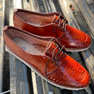 May include: A pair of brown leather shoes with woven detailing. The shoes have laces and a rounded toe.