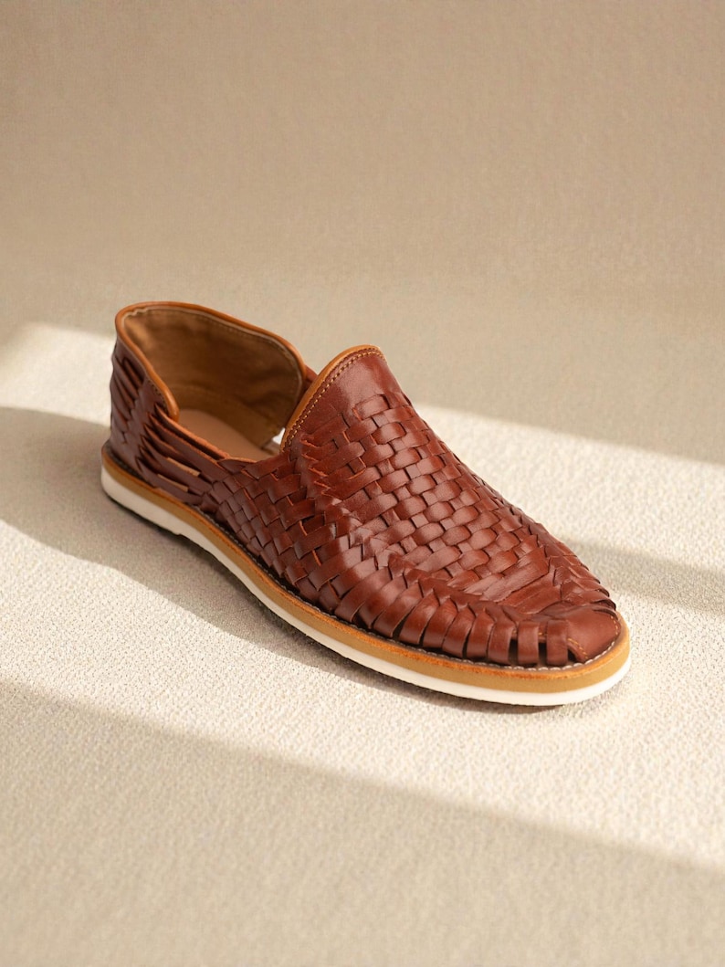 May include: A brown leather woven shoe with a white sole. The shoe has a low profile and a slip-on design. The woven pattern covers the top of the shoe.