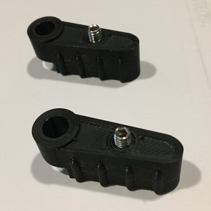 May include: Two black plastic parts with a threaded hole and a round hole. The parts have a textured surface and are designed to be attached to something.