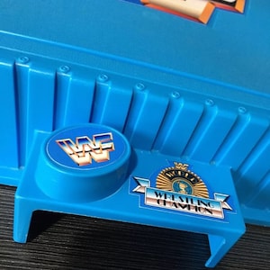 May include: Blue plastic wrestling ring toy with a WWF logo and "World Wrestling Champion" text.