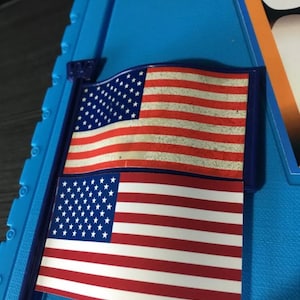 May include: Two American flags, one above the other, on a blue background. The top flag is faded and the bottom flag is new.