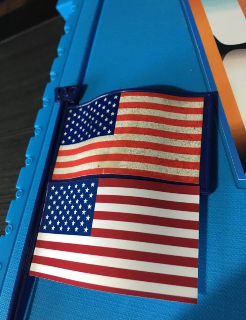 May include: Two American flags, one above the other, on a blue background. The top flag is faded and the bottom flag is new.