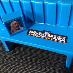 May include: A blue plastic wrestling ring playset with a wrestler figure and a "WWF Wrestlemania" logo sticker.