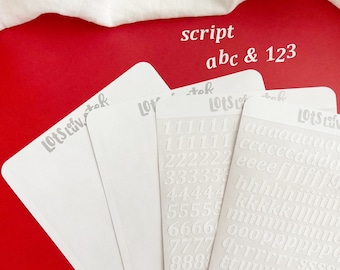 May include: Four white sticker sheets featuring embossed letters and numbers in a script font. The sheets display the text 'Lots of luv, stef' at the top. One sheet contains rows of lowercase alphabet letters, another shows columns of numbers 0 through 9.