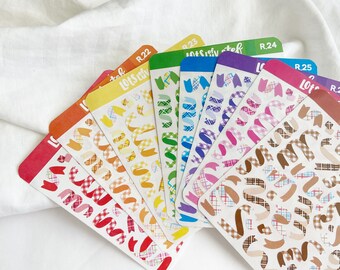 Puede incluir: Un conjunto de diez hojas de pegatinas de colores con un patrón de cuadros y una variedad de diseños de cintas. Las hojas de pegatinas están etiquetadas con el texto "LotS" y un número del 22 al 26.