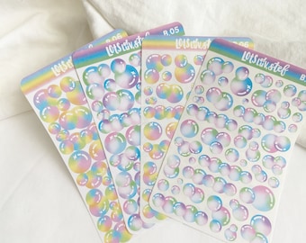 Puede incluir: Cuatro hojas de pegatinas de burbujas de colores arcoíris. Cada hoja tiene una variedad de tamaños y formas de burbujas con una estrella blanca en el centro. El texto "Lots Luv. etc." está impreso en cada hoja.