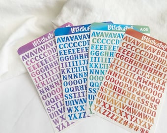 Puede incluir: Cuatro hojas de pegatinas de alfabeto con un fondo degradado arcoíris. Las letras están en una fuente retro en negrita. Las hojas están etiquetadas como "Lots Liv, stef" y "Lots Liv, stol".