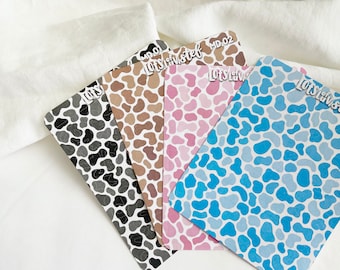Puede incluir: Cuatro hojas de papel estampado con un diseño de estampado de vaca. Las hojas son en blanco y negro, marrón, rosa y azul.