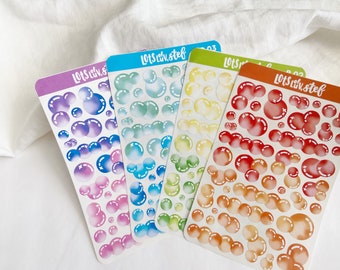 Puede incluir: Cuatro hojas de pegatinas de burbujas de colores con un degradado arcoíris. Cada hoja tiene un degradado de color diferente, incluyendo rosa, azul, verde y naranja. Las pegatinas presentan burbujas de diferentes tamaños con una estrella blanca en el centro.