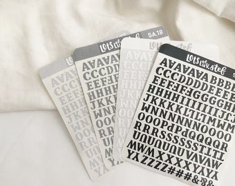 Puede incluir: Cuatro hojas de pegatinas de alfabeto con letras en blanco y negro. Las hojas están etiquetadas como "Lots of Love" y "Lots Liv. stef".