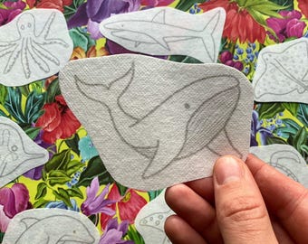 May include: A set of iron-on patches featuring various sea creatures, including an octopus, a whale, a shark, a stingray, and a dolphin. The patches are white with black outlines and are on a floral background.