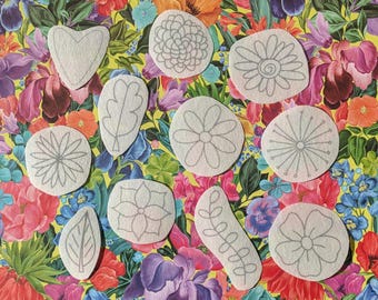 May include: A selection of light-coloured fabric patches in diverse shapes, such as flowers, leaves, and hearts, featuring grey line drawings. The patches are set against a vibrant floral backdrop with a mix of pink, purple, orange, and blue flowers.
