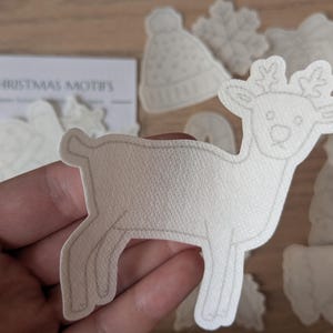 May include: A selection of white Christmas motifs, including a reindeer, a hat, and snowflakes. The reindeer is the main focus, with a detailed outline. The text "CHRISTMAS MOTIFS" is visible on a card in the background.