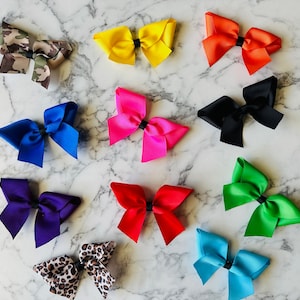 May include: Twelve different colored hair bows, including camouflage, yellow, orange, black, pink, blue, purple, green, light blue, and leopard print.