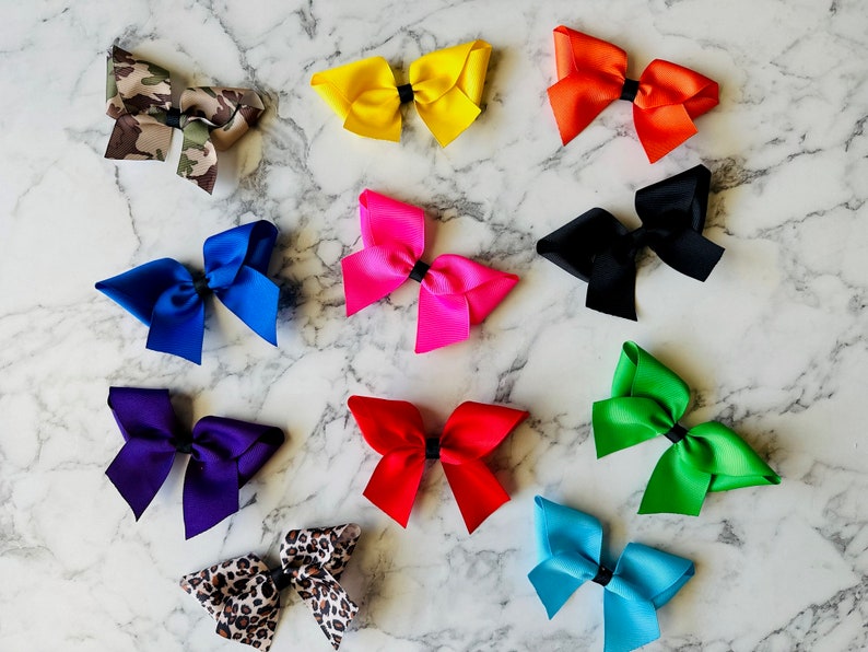 May include: Twelve different colored hair bows, including camouflage, yellow, orange, black, pink, blue, purple, green, light blue, and leopard print.