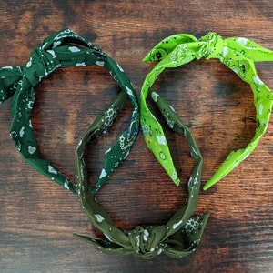 May include: Two fabric headbands with a knotted design. One headband is green with a white paisley pattern and the other is lime green with a white paisley pattern.
