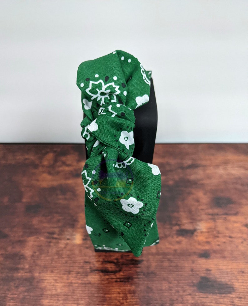 May include: Green headband with a white and black bandana print. The headband is tied in a knot at the top.