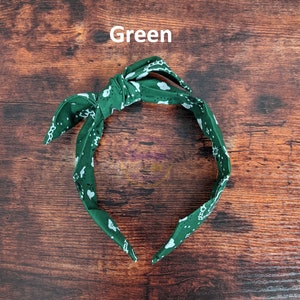 May include: Green headband with a white paisley pattern. The headband is tied in a knot at the top.