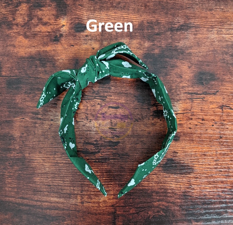 May include: Green headband with a white paisley pattern. The headband is tied in a knot at the top.