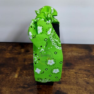 May include: Green bandana headband with a white paisley pattern. The headband is tied in a knot at the top.