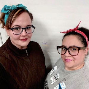 May include: Two women wearing headbands with a bow. The woman on the left is wearing a teal headband with a white and blue pattern. The woman on the right is wearing a red headband with a white pattern. Both women are wearing glasses.