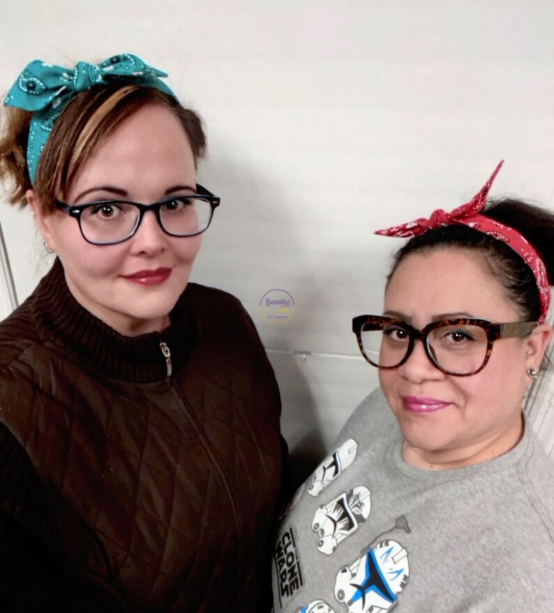 May include: Two women wearing headbands with a bow. The woman on the left is wearing a teal headband with a white and blue pattern. The woman on the right is wearing a red headband with a white pattern. Both women are wearing glasses.