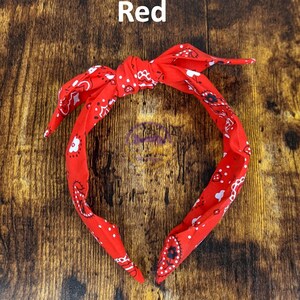 May include: Red bandana headband with a white paisley pattern. The headband is tied in a knot at the top.