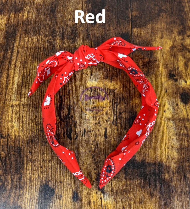 May include: Red bandana headband with a white paisley pattern. The headband is tied in a knot at the top.