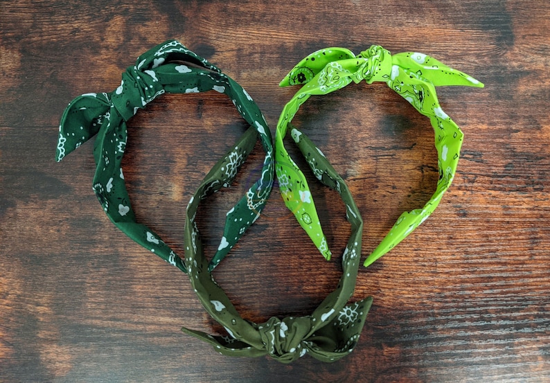 May include: Two fabric headbands with a knotted design. One headband is green with a white paisley pattern and the other is lime green with a white paisley pattern.