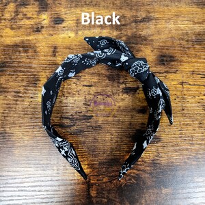 May include: Black bandana headband with a white paisley pattern. The headband is tied in a knot at the top.