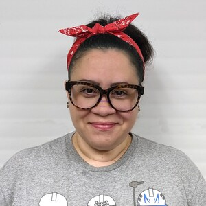 May include: A woman wearing a grey t-shirt with a Star Wars themed graphic print. She is wearing a red bandana headband and brown framed glasses.