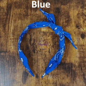 May include: Blue bandana headband with a white paisley pattern. The headband is tied in a knot at the top.