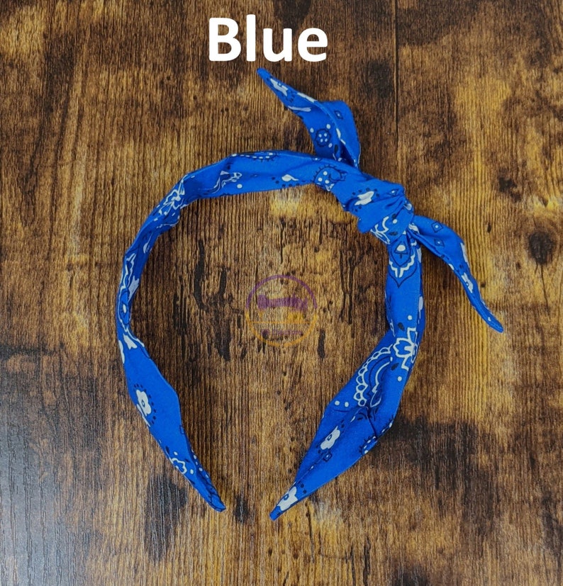 May include: Blue bandana headband with a white paisley pattern. The headband is tied in a knot at the top.