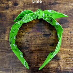 May include: A lime green bandana headband with a white paisley pattern. The headband is tied in a knot at the top.