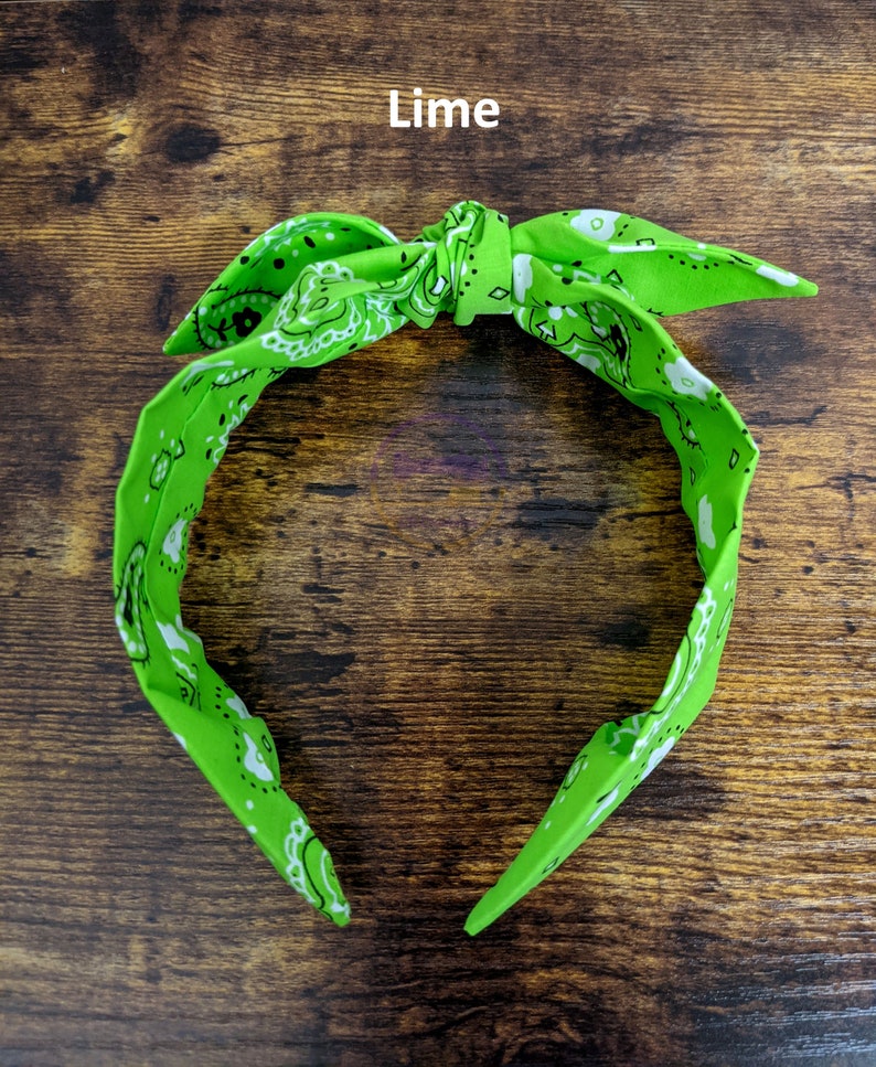 May include: A lime green bandana headband with a white paisley pattern. The headband is tied in a knot at the top.